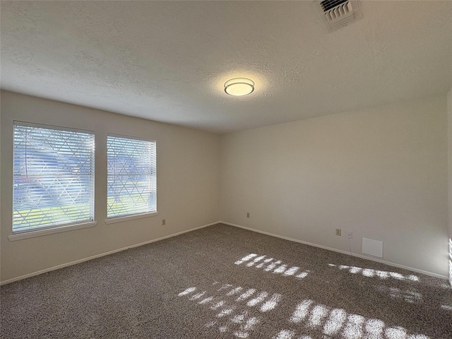 empty room with a healthy amount of sunlight, dark carpet, visible vents, and a textured ceiling