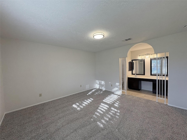 unfurnished living room featuring baseboards, visible vents, arched walkways, light colored carpet, and a textured ceiling