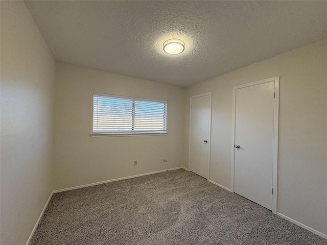 unfurnished bedroom with a textured ceiling, carpet flooring, and baseboards