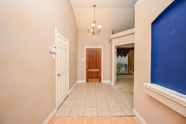 entrance foyer featuring a chandelier, vaulted ceiling, light wood-style flooring, and baseboards