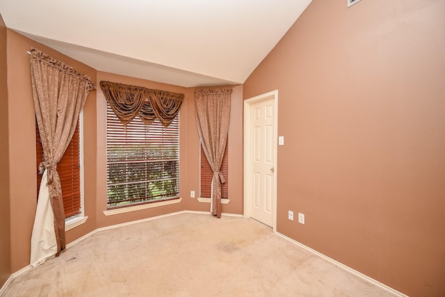 spare room featuring lofted ceiling, carpet flooring, and baseboards