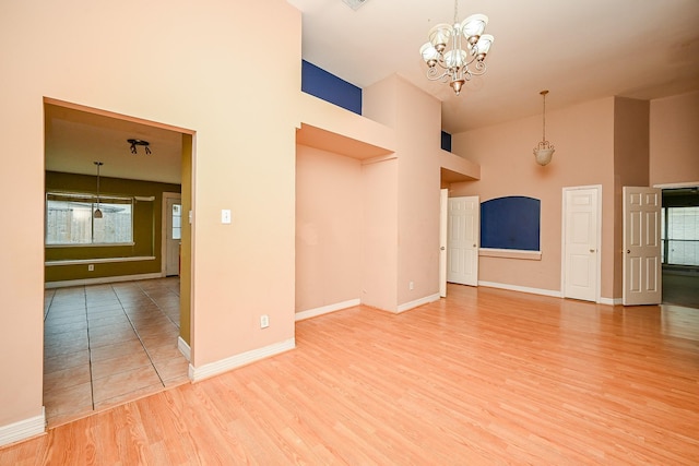 unfurnished living room with a towering ceiling, baseboards, a chandelier, and wood finished floors