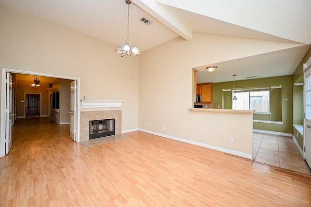 unfurnished living room with visible vents, a tiled fireplace, light wood-style floors, a chandelier, and beamed ceiling