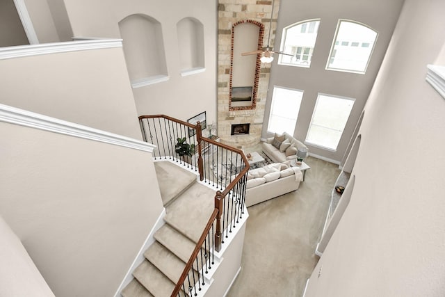 stairway with a towering ceiling, ceiling fan, carpet, and a stone fireplace