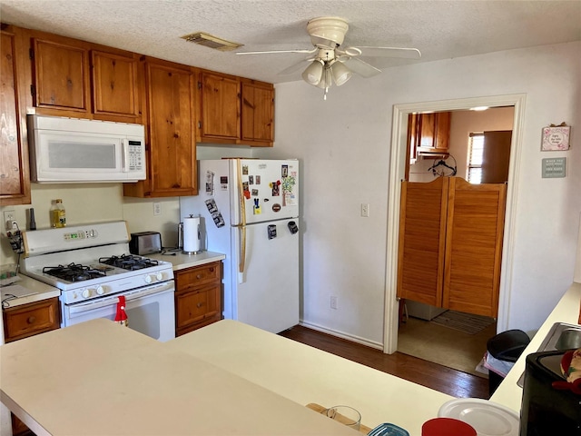 kitchen with white appliances, visible vents, and brown cabinets