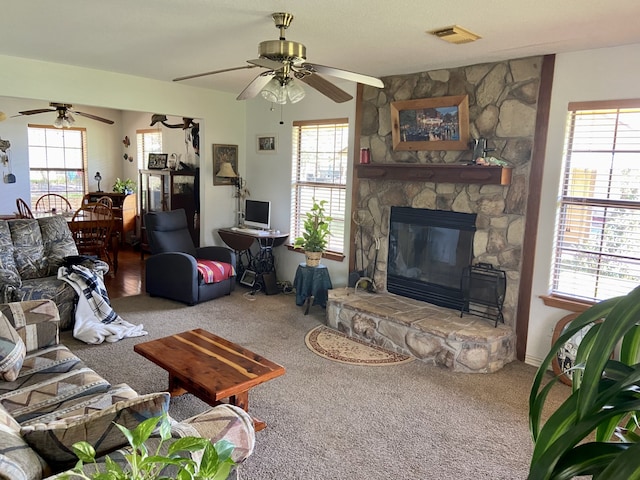 living area featuring carpet floors, a stone fireplace, visible vents, and a ceiling fan