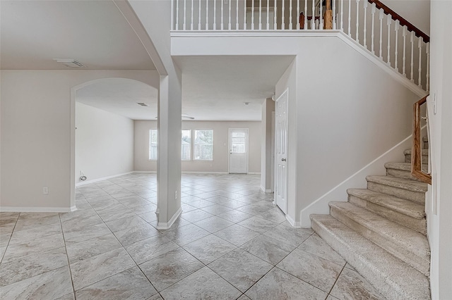 entryway featuring arched walkways, light tile patterned flooring, baseboards, and stairs