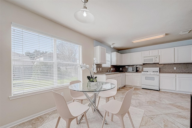 kitchen with white appliances, visible vents, white cabinets, hanging light fixtures, and decorative backsplash