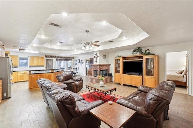 living room featuring a tray ceiling, visible vents, a fireplace, and light wood finished floors