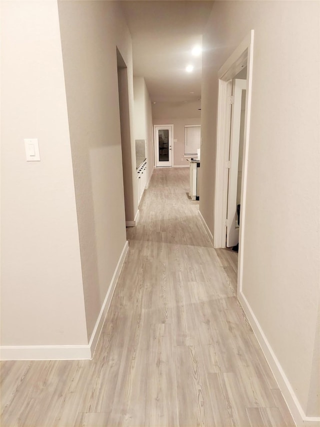 hallway featuring light wood-style flooring and baseboards