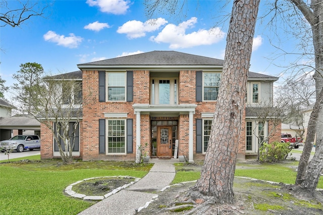 view of front of house featuring roof with shingles, brick siding, and a front lawn