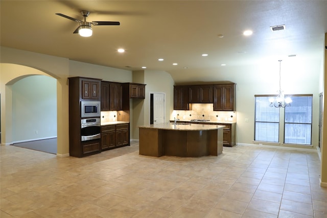 kitchen featuring pendant lighting, visible vents, appliances with stainless steel finishes, a kitchen island with sink, and ceiling fan with notable chandelier