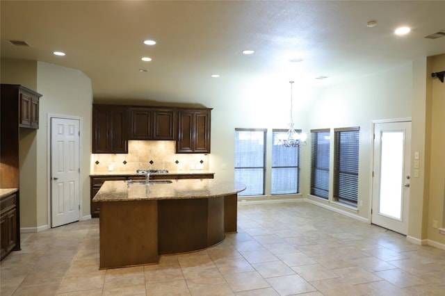 kitchen with a kitchen island with sink, hanging light fixtures, visible vents, and light stone countertops