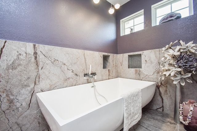 full bath featuring tile walls, a freestanding bath, and a textured wall