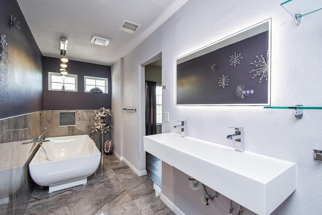 bathroom with a textured wall, a freestanding tub, a sink, visible vents, and marble finish floor