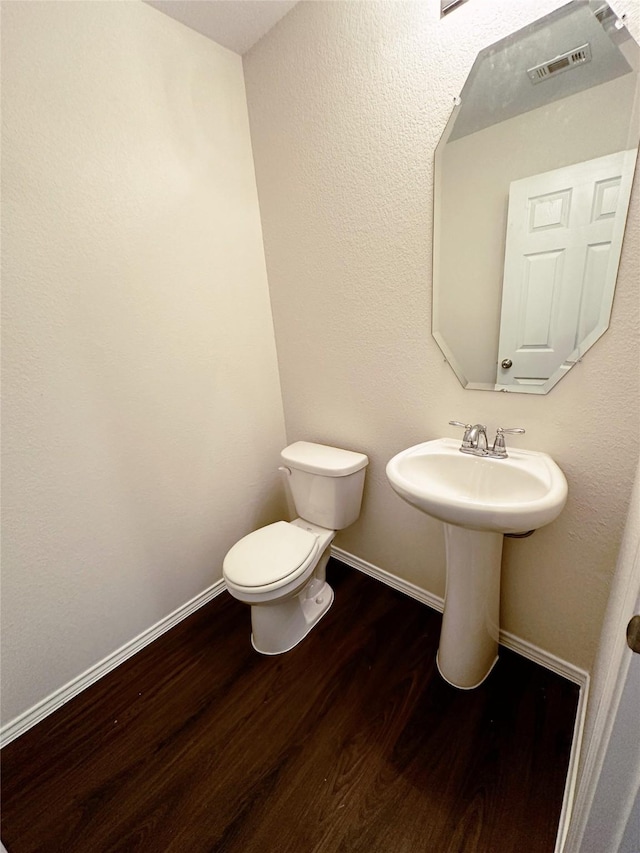 half bath featuring wood finished floors, toilet, and baseboards