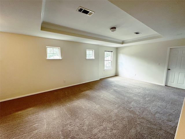 carpeted empty room with baseboards, visible vents, a raised ceiling, and ornamental molding