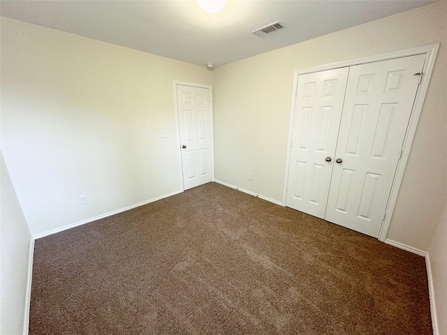 unfurnished bedroom with dark colored carpet, a closet, visible vents, and baseboards