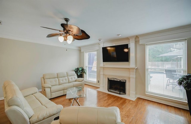 living area featuring baseboards, a ceiling fan, a premium fireplace, ornamental molding, and light wood-style floors