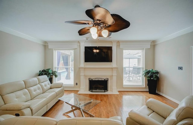 living room with ceiling fan, a fireplace, baseboards, light wood-style floors, and crown molding