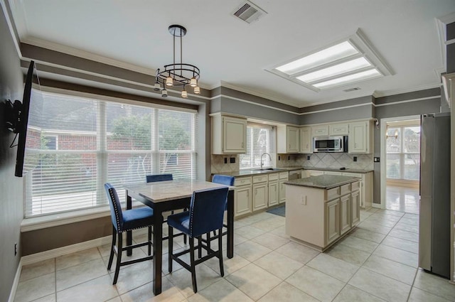 kitchen featuring visible vents, a kitchen island, appliances with stainless steel finishes, cream cabinets, and a sink