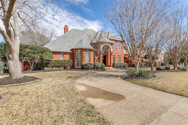 view of front of home with brick siding, concrete driveway, roof with shingles, a front lawn, and a chimney