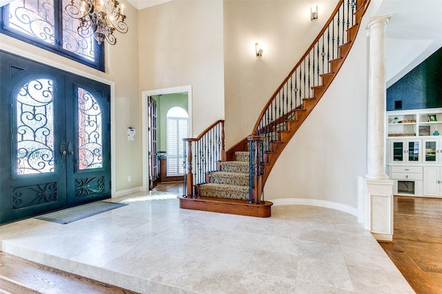 foyer featuring a high ceiling, baseboards, stairs, french doors, and ornate columns