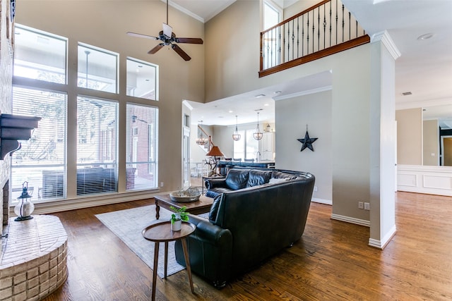 living area with baseboards, a ceiling fan, a towering ceiling, dark wood-type flooring, and crown molding