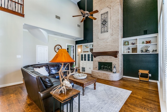 living room with ceiling fan, visible vents, baseboards, a brick fireplace, and dark wood finished floors