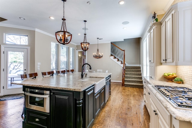 kitchen featuring pendant lighting, a center island with sink, appliances with stainless steel finishes, a sink, and dark cabinetry