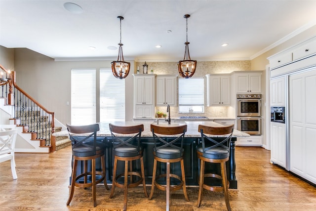 kitchen featuring a kitchen breakfast bar, decorative light fixtures, a kitchen island with sink, light wood-style floors, and double oven