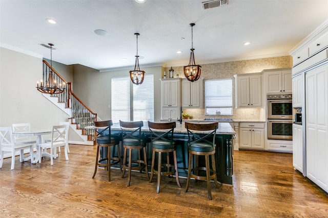 kitchen with light stone counters, a kitchen island with sink, a kitchen breakfast bar, hanging light fixtures, and appliances with stainless steel finishes