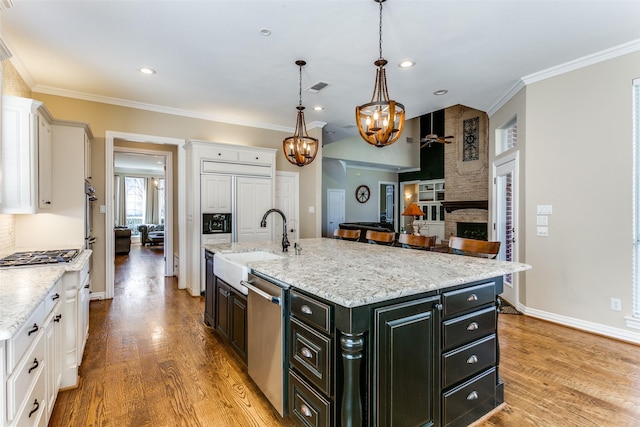 kitchen with decorative light fixtures, stainless steel appliances, light wood-style flooring, white cabinetry, and an island with sink