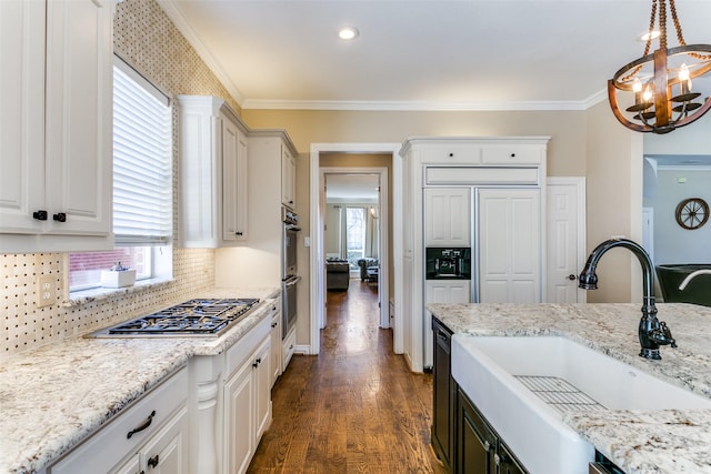 kitchen featuring decorative light fixtures, crown molding, appliances with stainless steel finishes, white cabinets, and a sink