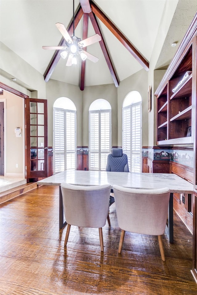 dining room featuring lofted ceiling with beams, a ceiling fan, wood finished floors, and wainscoting