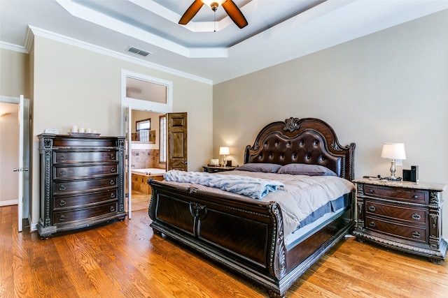 bedroom featuring ornamental molding, a tray ceiling, wood finished floors, and visible vents