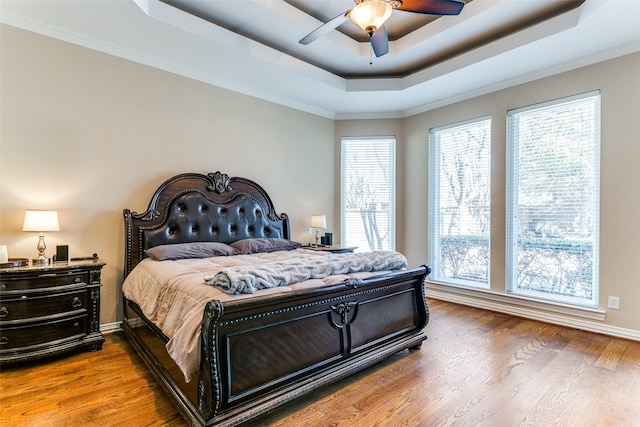 bedroom with a raised ceiling, ceiling fan, baseboards, and wood finished floors