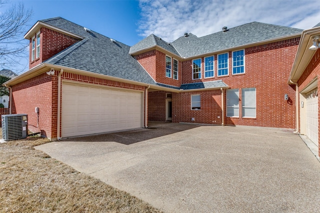 traditional-style home featuring roof with shingles, brick siding, central AC, a garage, and driveway