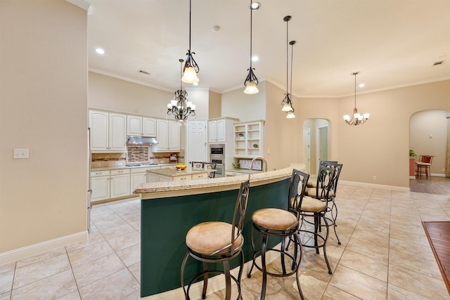 kitchen featuring arched walkways, white cabinets, a large island, light stone countertops, and pendant lighting