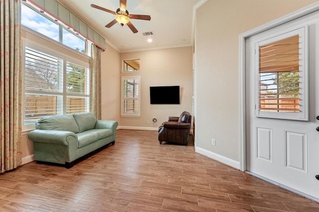 living area featuring light wood-type flooring, baseboards, ornamental molding, and a ceiling fan