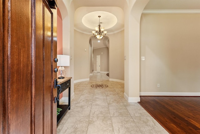 hall with arched walkways, a chandelier, baseboards, light wood-type flooring, and crown molding