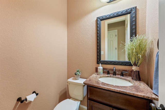 half bathroom with a textured wall, vanity, and toilet