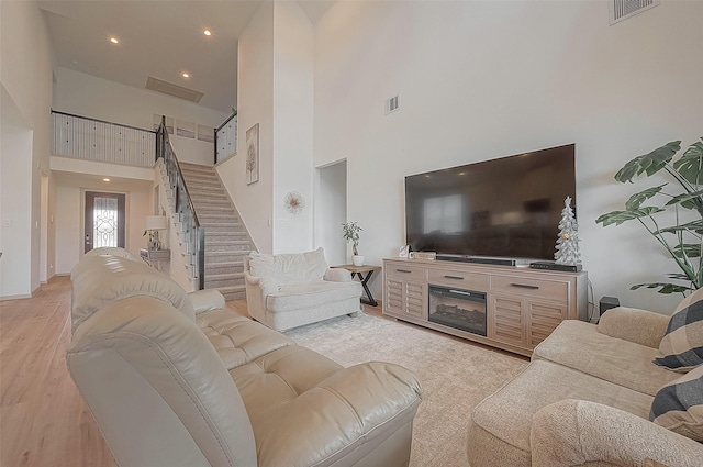 living room featuring a high ceiling, light wood finished floors, stairway, and visible vents