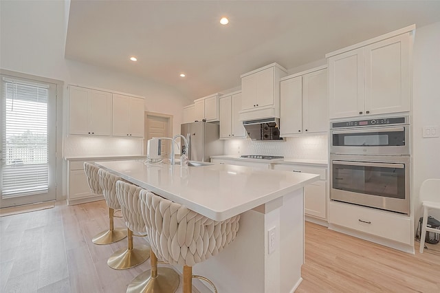 kitchen with white cabinets, a kitchen island with sink, stainless steel appliances, light countertops, and a kitchen bar