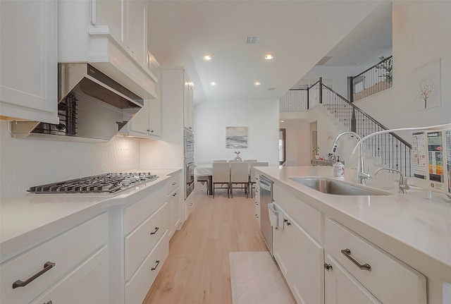 kitchen with a sink, white cabinets, light countertops, appliances with stainless steel finishes, and light wood-type flooring