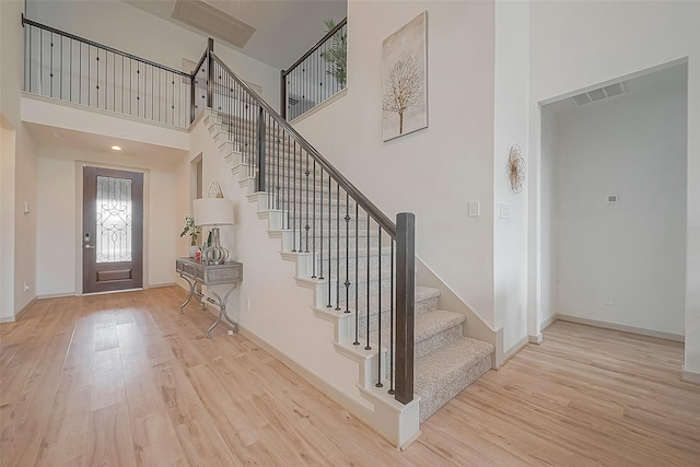 foyer with a high ceiling, baseboards, visible vents, and light wood finished floors