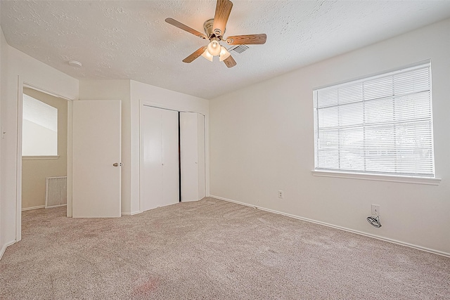 unfurnished bedroom featuring a textured ceiling, ceiling fan, a closet, and light colored carpet