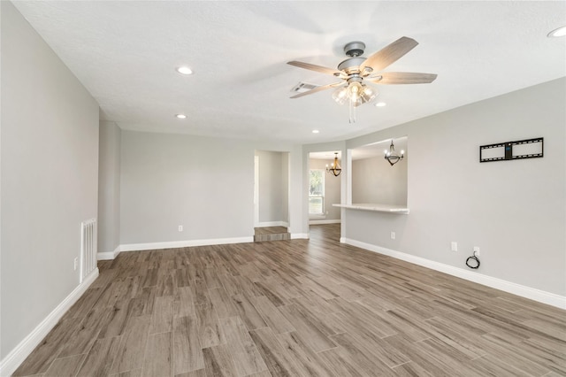 spare room featuring visible vents, ceiling fan with notable chandelier, light wood-style flooring, and baseboards