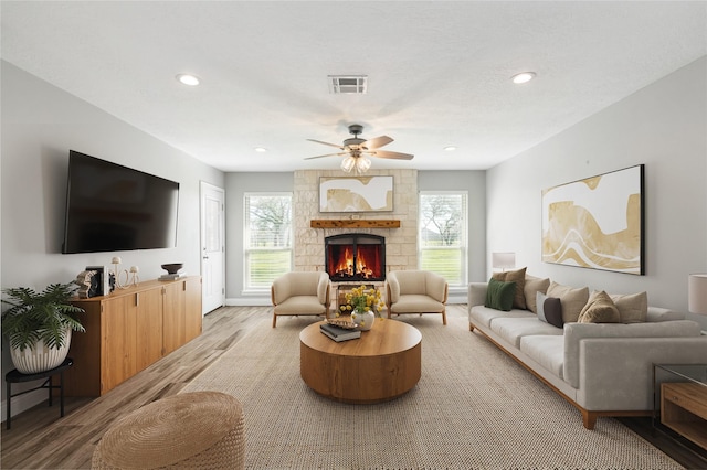 living area featuring recessed lighting, visible vents, ceiling fan, a stone fireplace, and wood finished floors