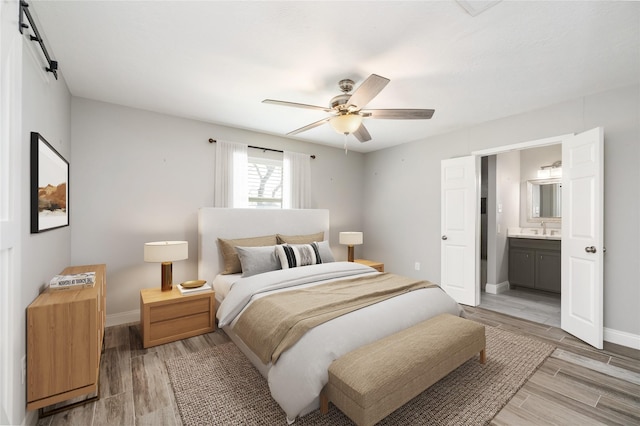 bedroom with a barn door, a sink, baseboards, light wood-type flooring, and ensuite bath